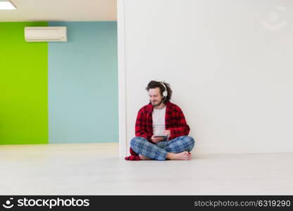 Young handsome man enjoying music through headphones,sitting on the floor at home