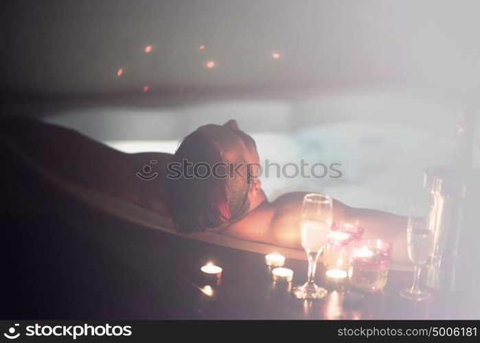 young handsome man enjoys relaxing in the jacuzzi with candles and champagne at luxury resort spa