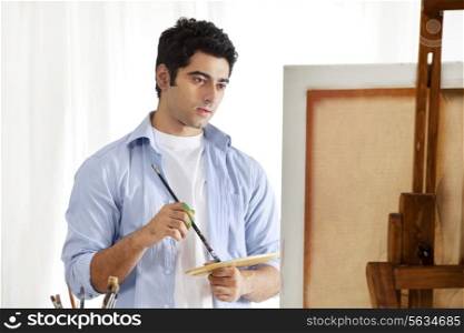 Young handsome man holding palette and paintbrush while painting