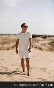 Young handsome man in light clothing and sunglasses in the desert. Concept of freedom relaxation. Place for text or advertising.. Young handsome man in light clothing and sunglasses in the desert. Concept of freedom relaxation. Place for text or advertising