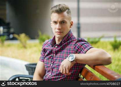 Young handsome man in plaid shirt on the background of summer street