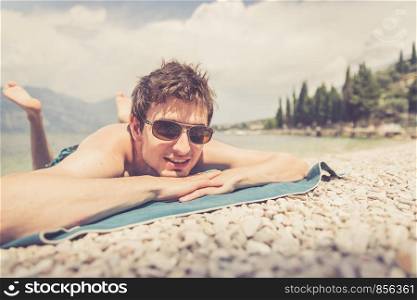 Young handsome man is lying on the beach, sun glasses