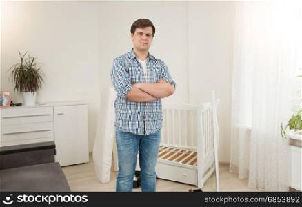 Young handsome man standing at disassembled baby crib