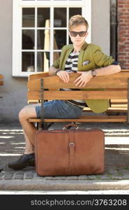 Young handsome man traveler casual style sitting on bench with suitcase waits, old town Gdansk Poland Europe