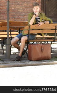 Young handsome man traveler casual style sitting on bench with suitcase waits, old town Gdansk Poland Europe