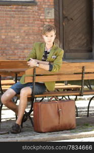 Young handsome man traveler casual style sitting on bench with suitcase waits, old town Gdansk Poland Europe