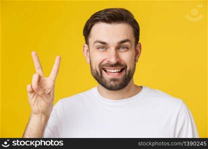 Young handsome man wearing striped t-shirt over isolated yellow background smiling looking to the camera showing fingers doing victory sign. Number two.. Young handsome man wearing striped t-shirt over isolated yellow background smiling looking to the camera showing fingers doing victory sign. Number two