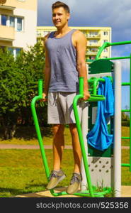 Young handsome man working out in outdoor gym. Sporty guy flexing his muscles doing sit ups on machine. Staying fit and healthy.. Man doing sit ups in outdoor gym