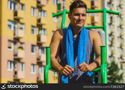 Young handsome man working out in outdoor gym, public park. Sporty guy about to exercise on machine. Staying fit and healthy.. Man working out in outdoor gym