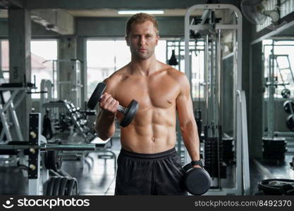 Young handsome muscular man working out with dumbbells. Strong bodybuilder in the gym fitness 