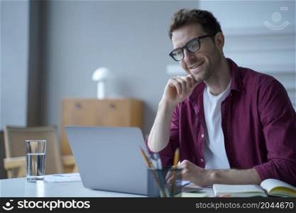 Young handsome smiling german man office worker in glasses enjoying video call on laptop computer, happy male employee in casual clothes talking with colleague during online conference. Young handsome smiling german man office worker in glasses enjoying video call on laptop computer