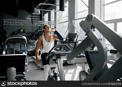 Young handsome sportsman drinking water from bottle during break after workout on treadmill running track. Fitness, healthy lifestyle concept. Sportsman drinking water during break after workout on treadmill running track