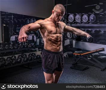 Young handsome sportsman lifting dumbbells in a gym. Sportsman lifting dumbbells