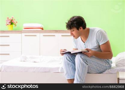 Young handsome student reading book in the bed 