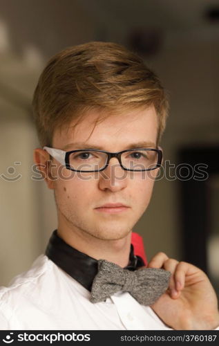 Young handsome stylish man fashion model in glasses wearing white shirt and bow tie posing indoor