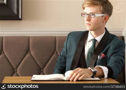 Young handsome stylish man fashion model thinking waiting in cafe /restaurant with his organizer