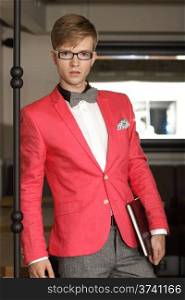 Young handsome stylish man fashion model wearning bright red jacket and bow tie with notebook posing indoor