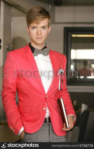 Young handsome stylish man fashion model wearning bright red jacket and bow tie with notebook posing indoor