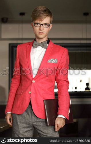 Young handsome stylish man fashion model wearning bright red jacket and bow tie with notebook posing indoor