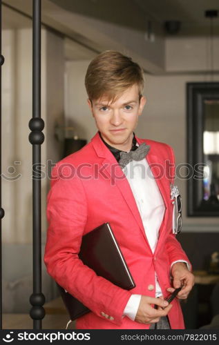 Young handsome stylish man fashion model wearning bright red jacket and bow tie with notebook posing indoor