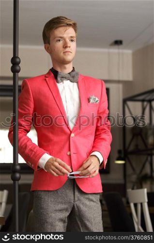 Young handsome stylish man fashion model wearning bright red jacket and bow tie posing indoor