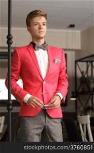 Young handsome stylish man fashion model wearning bright red jacket and bow tie posing indoor