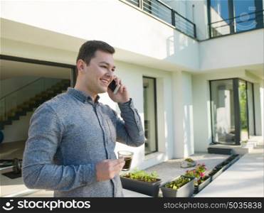 young handsome successful man using mobile phone in front of his luxury home villa