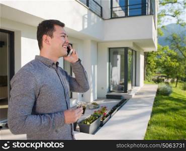young handsome successful man using mobile phone in front of his luxury home villa