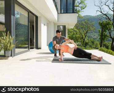 young handsome woman with personal trainer doing morning yoga exercises in front of her luxury home villa