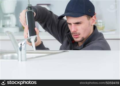 young handyman applying silicone sealant with gun around sink