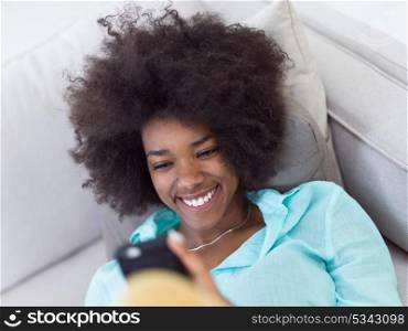 young happy african american woman sitting on sofa and using mobile phone at luxury home