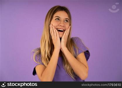 Young happy and surprised woman looking up and holding cheeks with hands while standing against isolated background.