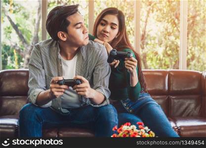 Young happy Asian couple playing video games in living room. Cheerful people having fun with computer gaming concept.