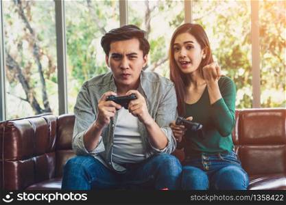 Young happy Asian couple playing video games in living room. Cheerful people having fun with computer gaming concept.