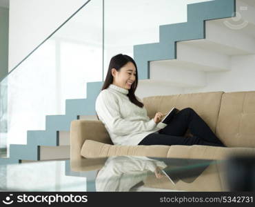 young happy asian woman sitting on sofa using Digital Tablet