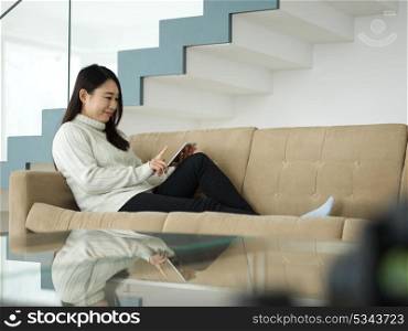 young happy asian woman sitting on sofa using Digital Tablet