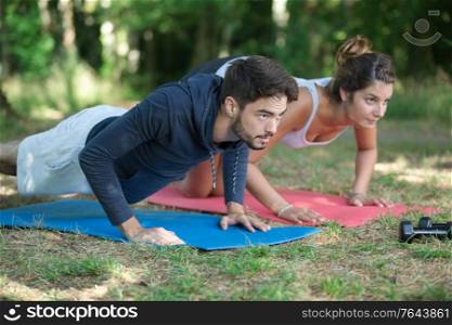 young happy athletic couple doing push-ups in park