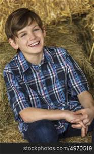 Young happy boy wearing a plaid shirt and sitting on bales of hay or straw with a toothy smile