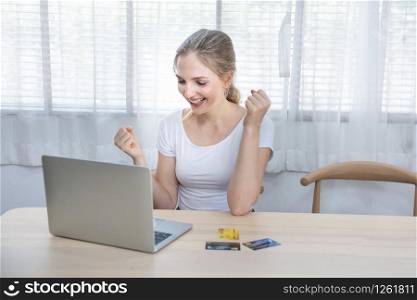 Young happy brunette caucasian woman in positive emotion on table with laptop and credit card,confortable wifi wireless technology shopping online at home with online application.