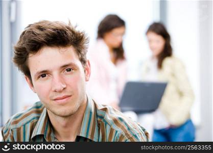 Young happy businessman looking at camera, smiling while business team working in background.