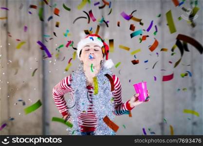 young happy casual business woman wearing a red hat and blowing party whistle while having new years confetti party in front of concrete wall