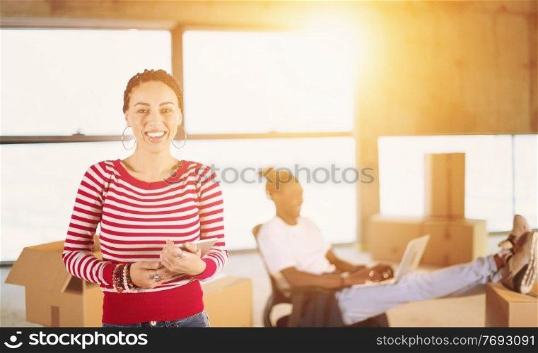 young happy casual modern muslim business woman using tablet computer on construction site with sunlight through the windows and african american colleague behind her during moving in at new startup office building