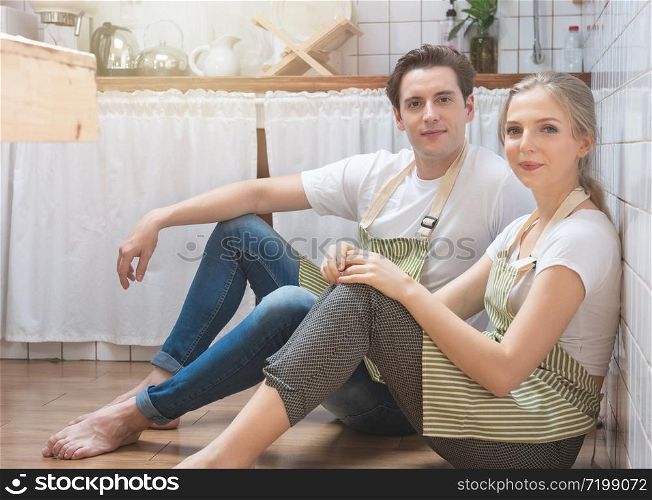 Young happy caucasian man and woman dress in lifestyle sitting on floor in kitchen and talking. Loving young couple spending time together at home.