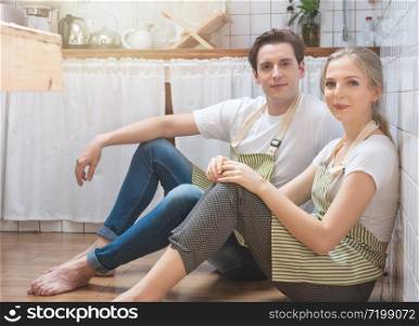 Young happy caucasian man and woman dress in lifestyle sitting on floor in kitchen and talking. Loving young couple spending time together at home.