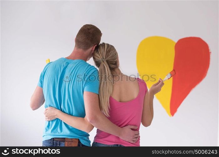 Young happy couple are painting a heart on the wall while doing repair at home.