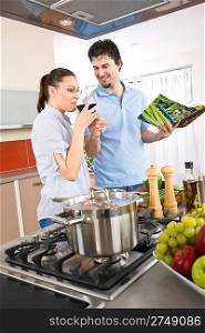 Young happy couple cook in kitchen with cookbook, pasta, vegetable