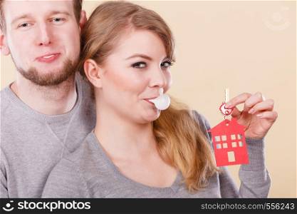 Young happy couple eating chewing gum while holding new house key with red home shape. Real estate housing family and happiness concept. . Funny couple holds keys to new home