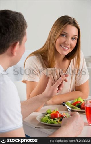 Young happy couple eating vegetable salad and holding each other hands