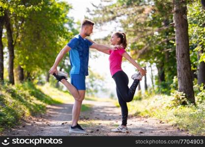 young happy couple enjoying in a healthy lifestyle warming up and stretching before jogging on a country road through the beautiful sunny forest, exercise and fitness concept