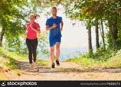 young happy couple enjoying in a healthy lifestyle while jogging on a country road through the beautiful sunny forest, exercise and fitness concept